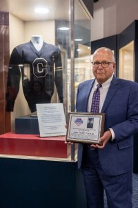 Mark Winzler, nephew of former UConn student-athlete John E. Winzler '42, holds a plaque commemorating John's induction to the Manchester (CT) Sports Hall of Fame while standing next to his uncle's athletic letter sweater that he donated to the Husky Heritage Sports Museum in the Alumni Center