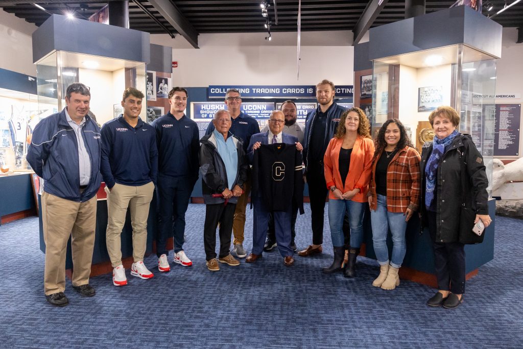 Attendees of the donation of athletic letter sweater that belonged to former UConn student-athlete John E. Winzler '42 to the Husky Heritage Sports Museum pose for a photo in the museum in the Alumni Center