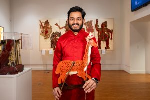 Rahul Koonathara, curator of the "Tradition and Revolution in Indian Shadow Puppetry" exhibition currently on display in the Ballard Institute and Museum, poses for a photo with one of the puppets in the exhibit