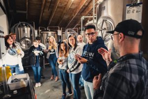 Faculty members and students stand in a brewery and listen to the brewer discuss varieties of hops.