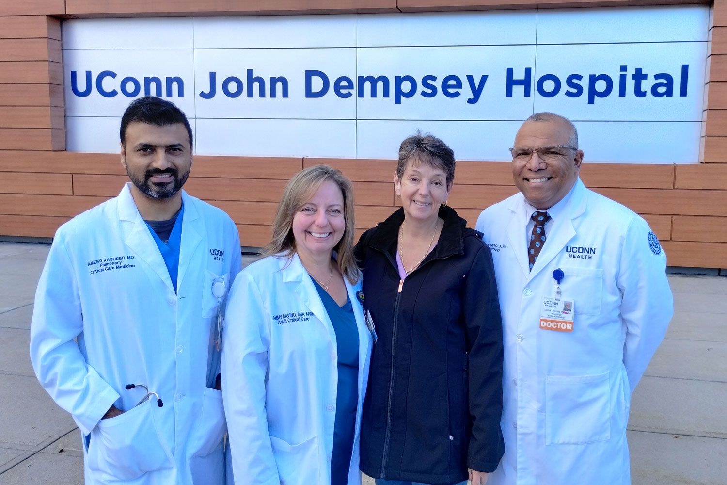 Group portrait of four in front of outdoor "UConn John Dempsey Hospital" sign.