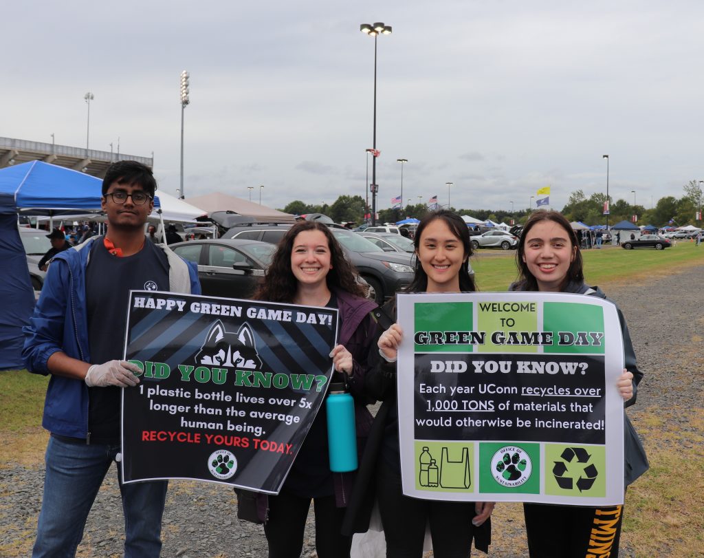 4 UConn students share recycling facts on posters outside a football stadium.