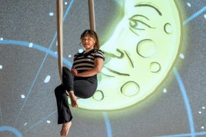 Abigail Baird '24 MFA sits on her aerial silk next to a projection of the moon during rehearsal for her one-woman show "Nothing Really Matters" in the Harriet Jorgensen Theatre 