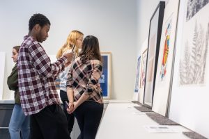 Students in professor Enrique Figueredo's Printmaking Workshop class (ART 3530) observe and discuss some of the artwork put on display by Assistant Curator and Academic Liaison for University Learning Amanda Douberley in the Benton Museum of Art's new Education Space 