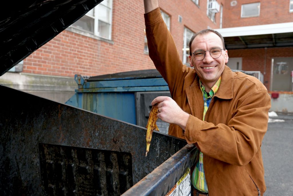 Man hold banana peel near dumpster