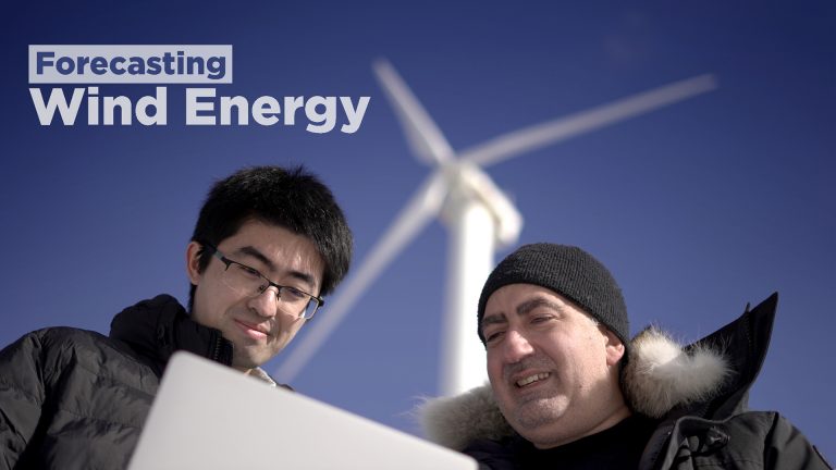 A researcher and student looking at data with a wind turbine in the background