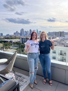 Two UConn graduate students stand together with the Dallas skyline behind them.