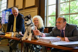 Jonathan XV sits on a table in front of Andy Bassett '75 (CLAS), President Radenka Maric and Chair Dan Toscano '87 (BUS), after being introduced to the University community at a meeting of the Board of Trustees at the Wilbur Cross Building