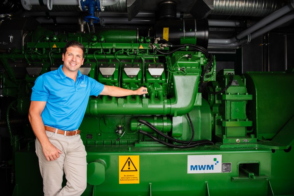 Alumnus Bryan Paganini stands in front of some of the equipment used by his sustainability-focused company, Quantum Biopower.