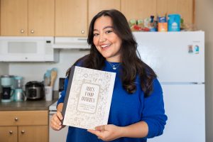 Arianna Melendez '24 poses with a copy of her cookbook, "Ari's Food Diaries," in her kitchen at Hilltop Apartments