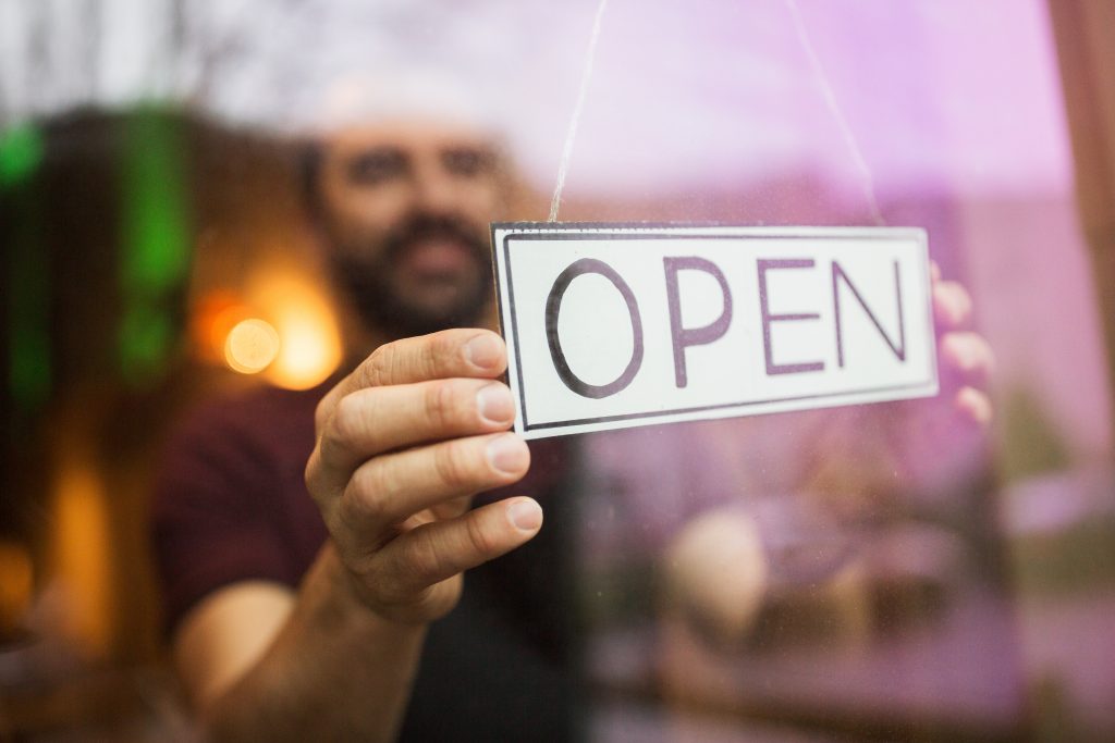 Owner of a small business hangs a sign that says "Open" in his shop window.