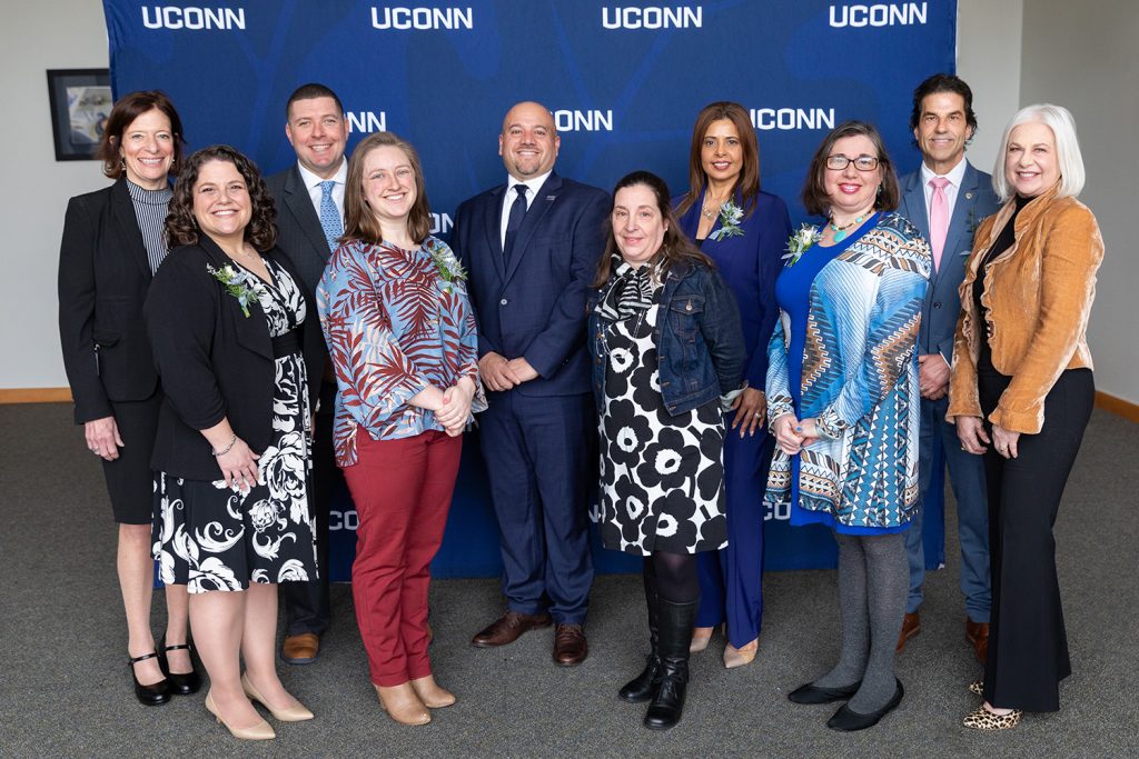 Neag School Alumni Award recipients gather in front of a blue UConn banner.
