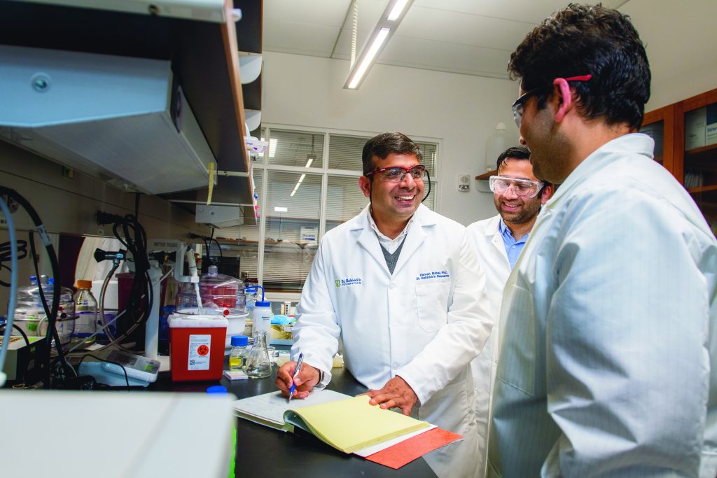 Three researchers in white lab coats in a lab writing something down on paper