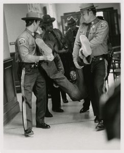 In an archival photo, a Black student is carried out of the old Wilbur Cross Library by Connecticut State Police.