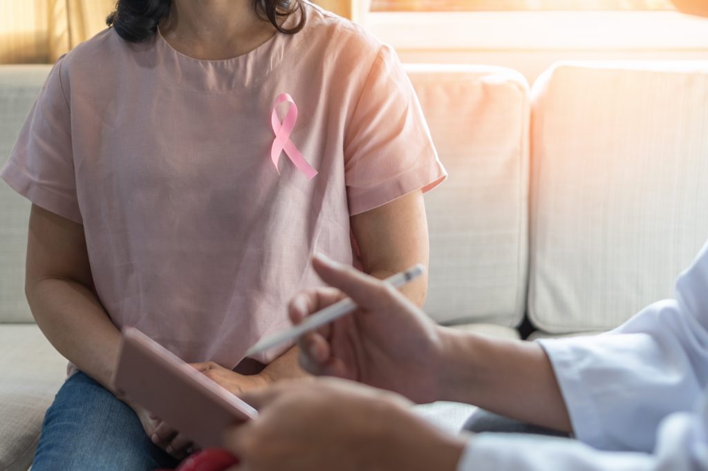 A woman wearing a pink ribbon for breast cancer awareness meets with a physician.