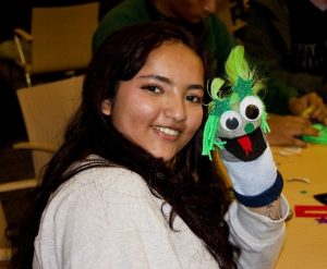 A female college student holds up a sock puppet.