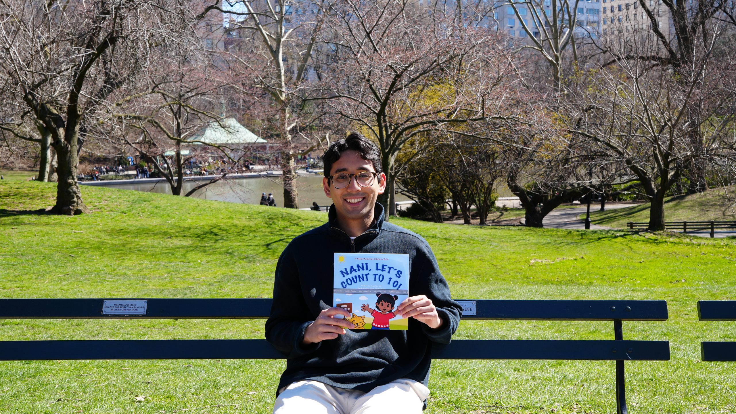 UConn alum Prabhas KC sits on a bench with a copy of the children's book he recently published.