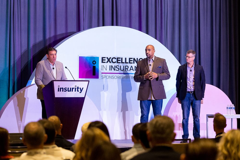 Three executives from Insurity on stage, presenting at a leadership conference.