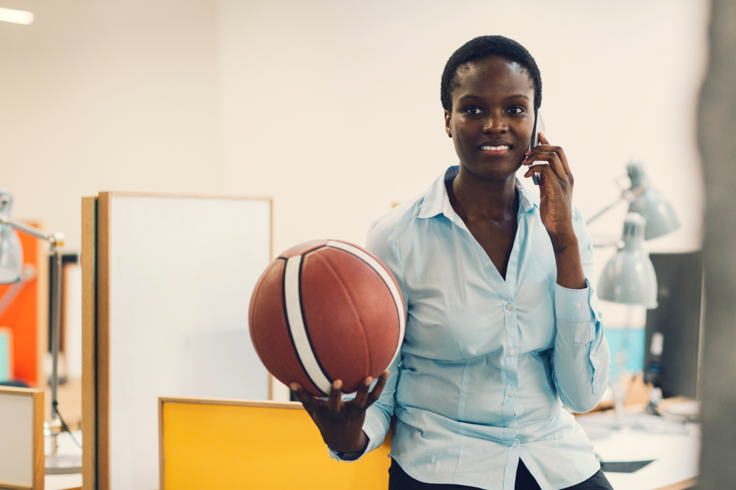 Professional African American women speaks on the phone while holding basketball.