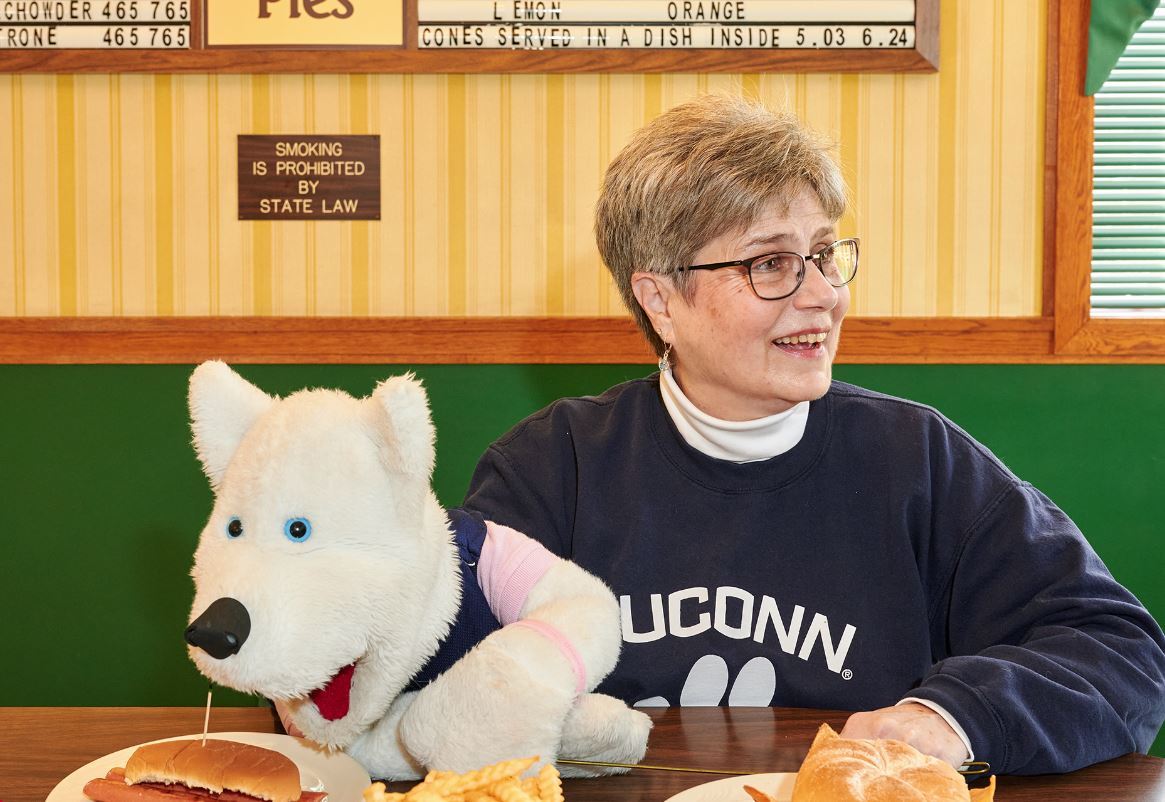 Carol McKenzie, a UConn basketball fans, sits in a restaurant with her white husky hand puppet, Jonathan Jr.