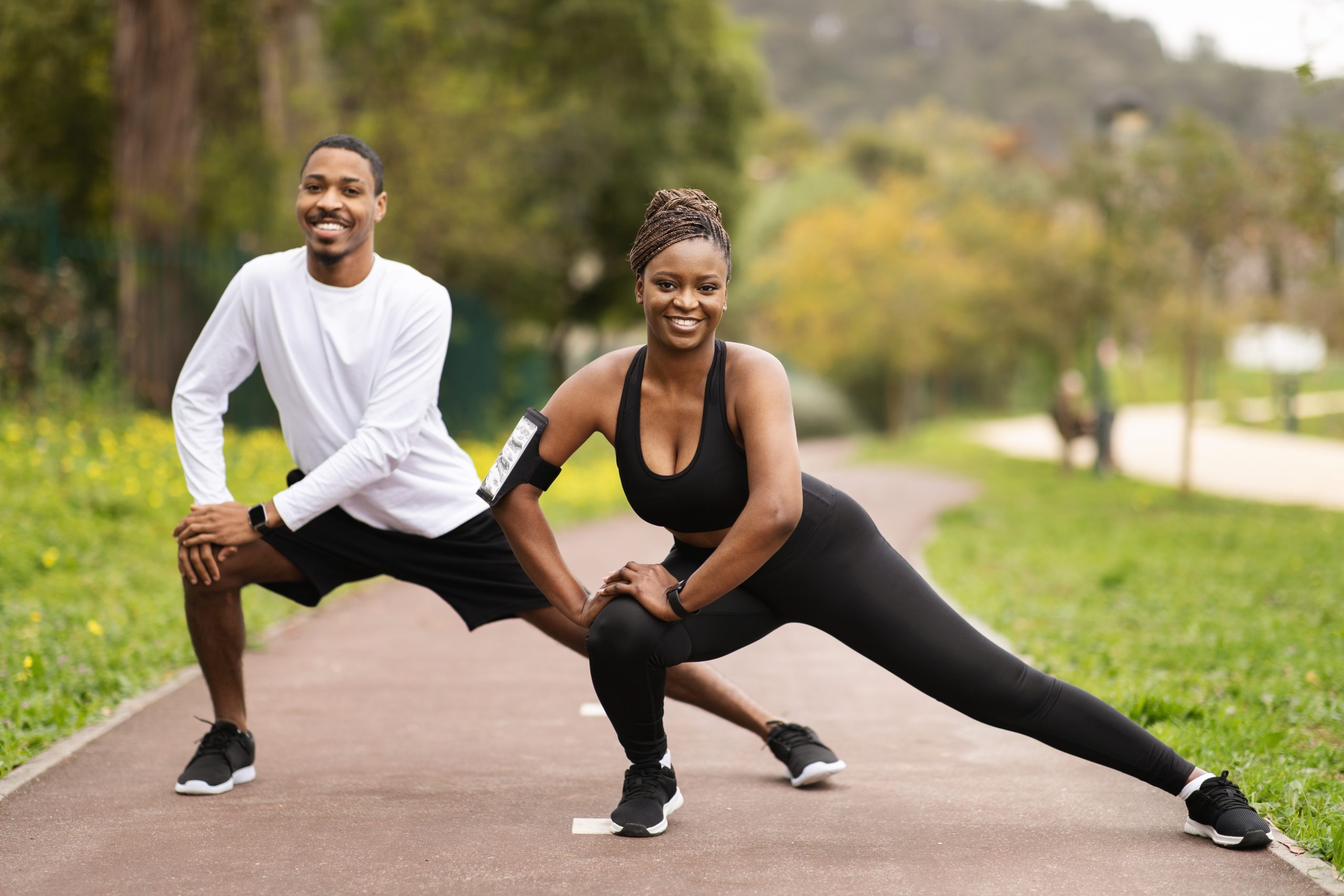 Young Black man and woman stretch their legs on a paved trail