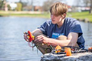 Oliver Mackinnon '25 looks at the small underwater robot prototype built by UConn's Underwater Robotics Club during a test run at Mirror Lake