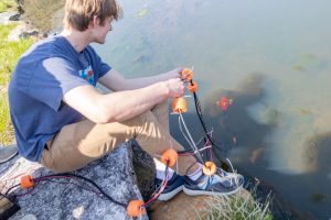 Oliver Mackinnon '25 handles the wiring to the small underwater robot prototype built by UConn's Underwater Robotics Club as it swims in Mirror Lake