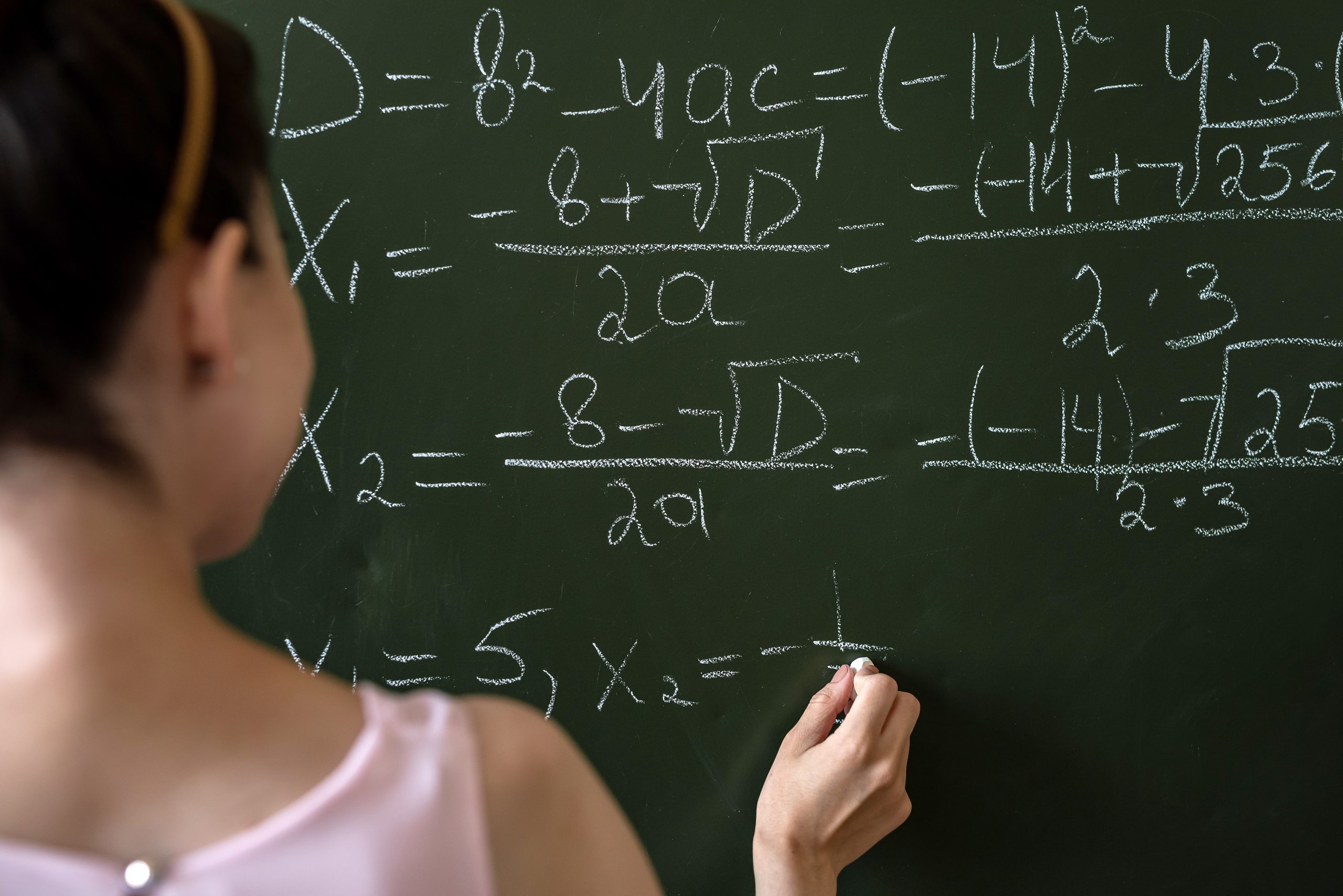 A young student writes math equations on a chalkboard.