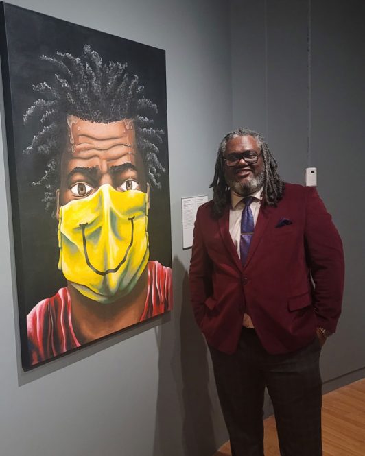 Andre Rochester standing beside his painting 'Wear Your Mask'