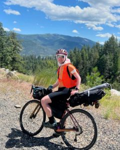 Matthew Fernandez on his bicycle with mountains in the background