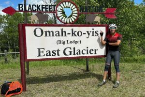 Jaydon Kinuthia next to a "Omah-ko-yis (Big Lodge) East Glacier" sign.