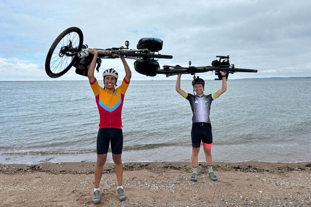 two men hoisting bicycles over their heads on a beach