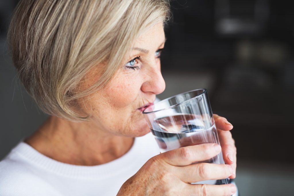 An older woman drinks water from a clear glass.