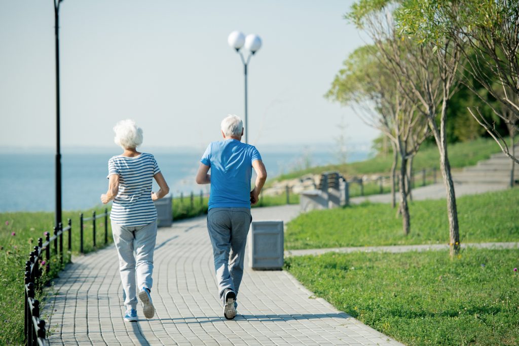 An older couple jogs along a seafront together.