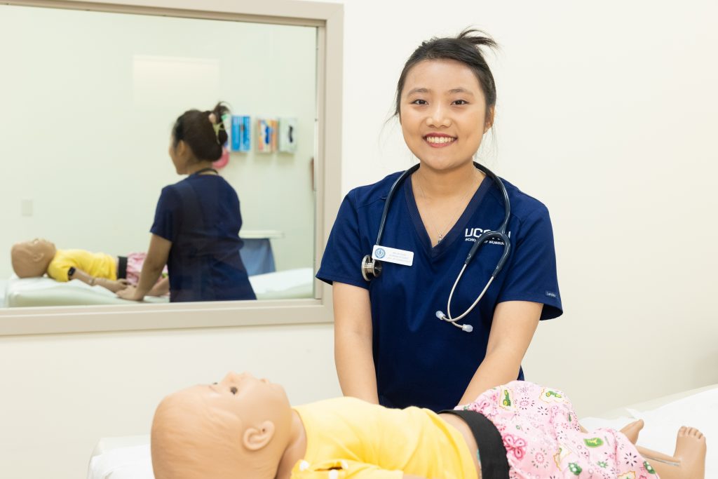 Meijin Hsiao '26 (NURS) poses for a photo with an infant-sized nursing manikin in one of the nursing simulation labs in the Widmer Wing of Storrs Hall