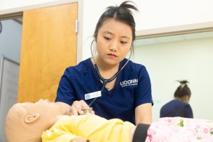 Meijin Hsiao '26 (NURS) listens to the heartbeat of an infant-sized nursing manikin in one of the nursing simulation labs in the Widmer Wing of Storrs Hall