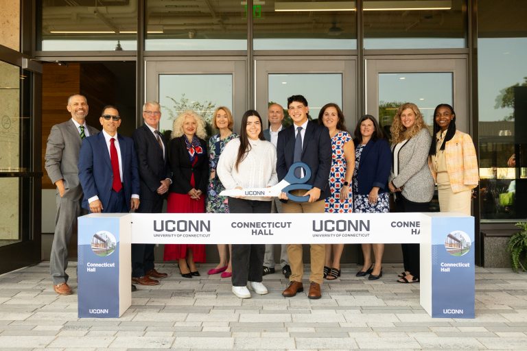 Senior resident assistants of Connecticut Hall Lauren Panza, center left, and Justin Guinta, center right, hold the scissors for the Connecticut Hall ribbon cutting among UConn leadership and Connecticut legislative members during a ceremony on Sept. 13, 2024.