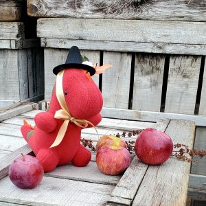 A stuffed dinosaur in a festive autumnal setting, with apples.