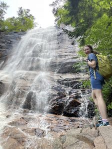 Sophia Hatzis wears a hiking backpack and smiles at the base of a waterfall.