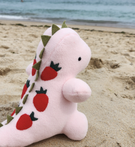 A Happy Dinosaur plush toy on a beach.