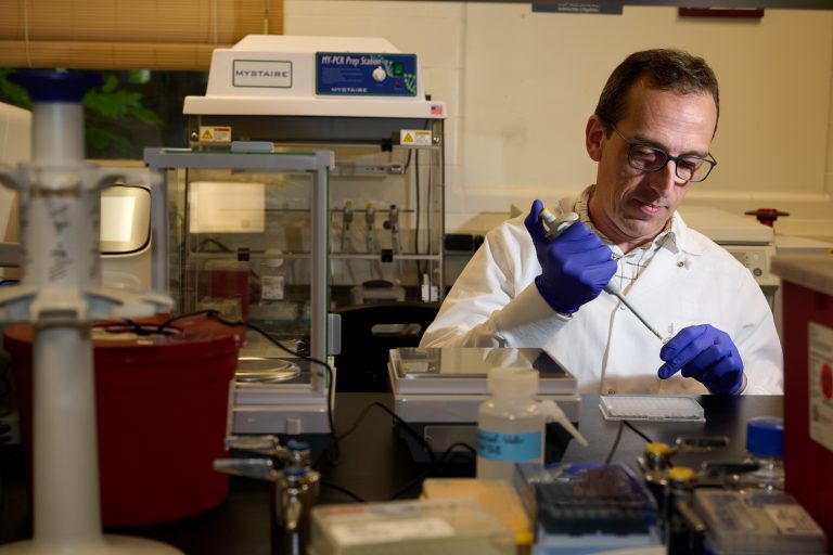 Elsio Wunder, a scientist wearing a labcoat and gloves draws liquid up into a pipette.