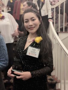 Zongjie Wang holding an award trophy, with a yellow rose pinned to her lapel