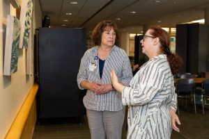 two women discussing art by paintings hung on nearby wall