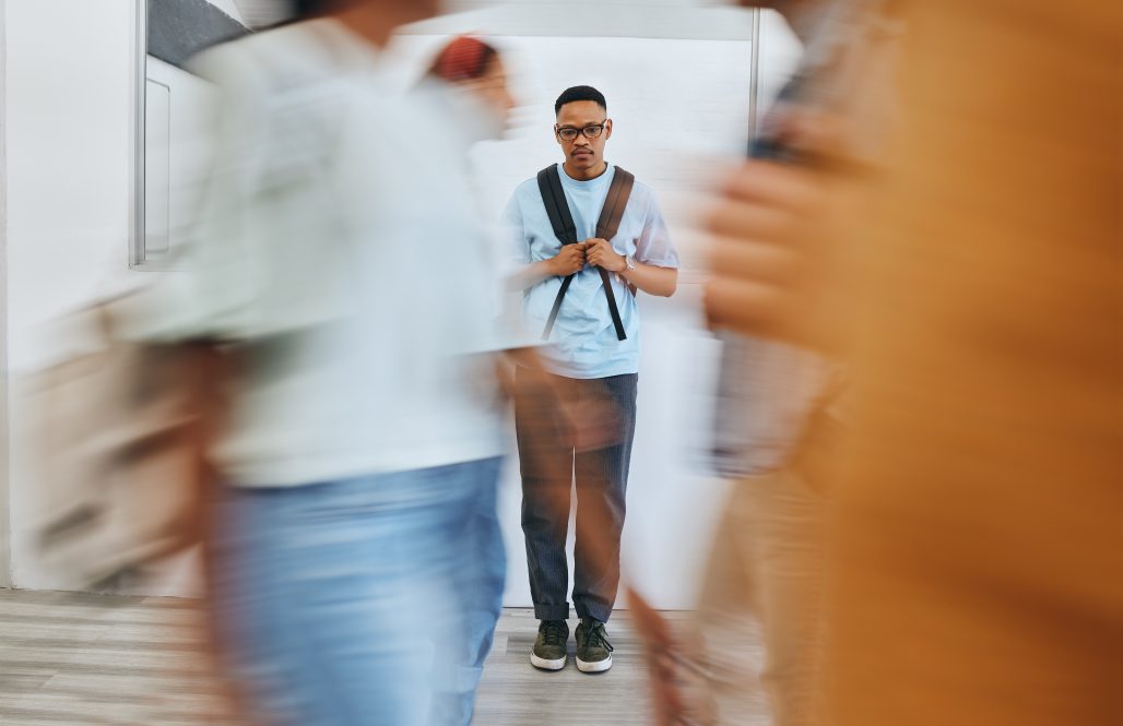 A college student stands isolated in the midst of activity.