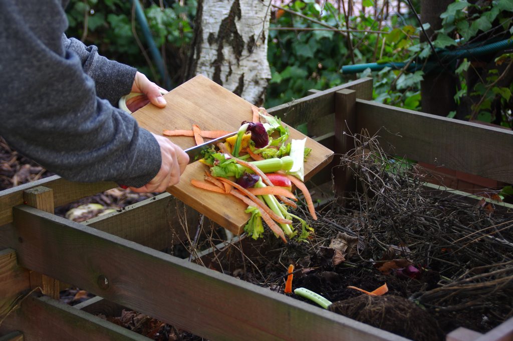 Ecology compost supply - kitchen waste recycling in backyard composter. The man throws leftover vegetables from the cutting board.