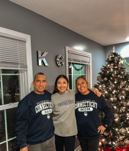 Vanessa Esquivel and her parents pose in front of a Christmas tree, wearing UConn sweatshirts.