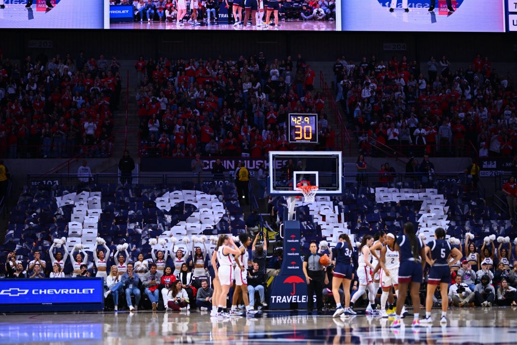 UConn Women's Basketball players on the court while the crowd holds up signs spelling out "1217"