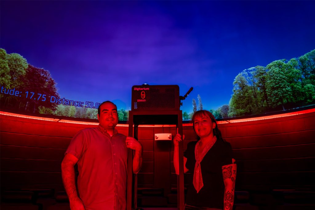 Matt Guthrie and PhD student Kelcey Davis pose next to the custom-built projector stand in the newly renovated Cynthia Wyeth Peterson Planetarium