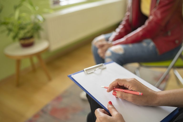 A female psychologist takes notes during a therapy meeting with a teenager in an office