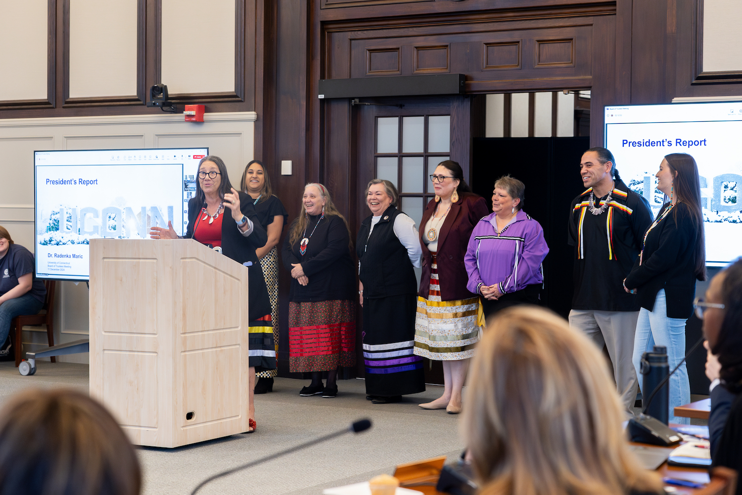 Beth Regan, chairwoman and justice of the Mohegan tribal nation, speaks during the UConn Board of Trustees' meeting as members of the Eastern Pequot, Golden Hill Paugussett, Mashantucket Pequot, Mohegan, and Schaghticoke tribal nations stand behind her in the North Reading Room of Wilbur Cross